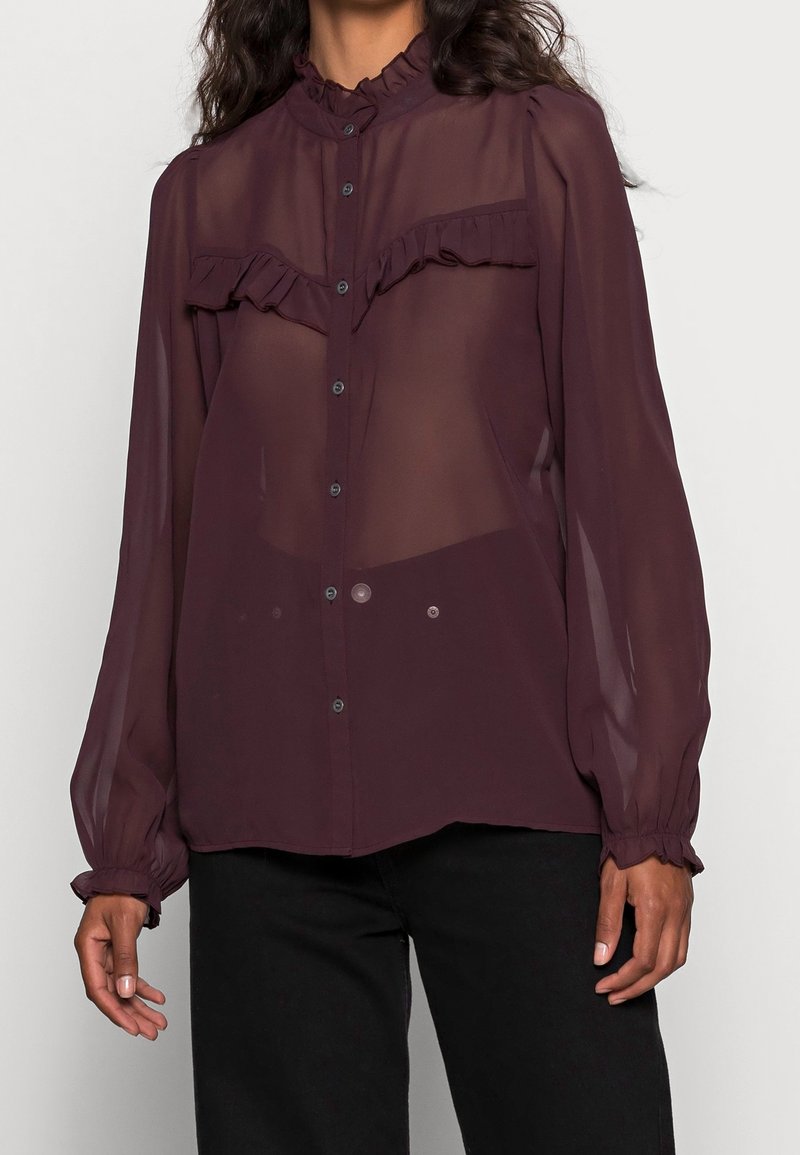 Gennemsigtig burgunderrød bluse med en flæsekrave og frontpanel; fulde ærmer med elastiske manchetter; diskrete knapdetaljer foran.