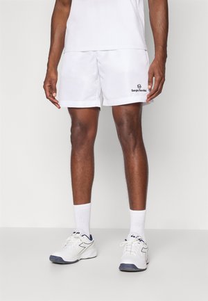 Shorts atletici bianchi con vita elastica, con un logo nero di "Sergio Tacchini" vicino all'orlo. Indossati con calzini bianchi e scarpe da ginnastica.
