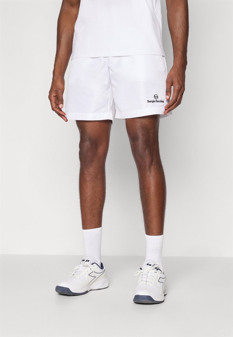 Biele športové šortky s elastickým pásom, s čiernym logom "Sergio Tacchini" blízko lemu. Doplnené o biele ponožky a tenisky.