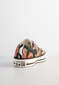 Baskets basses en toile avec un motif floral orange, vert et noir. Comprend une semelle en caoutchouc blanche avec des accents noirs et un logo.