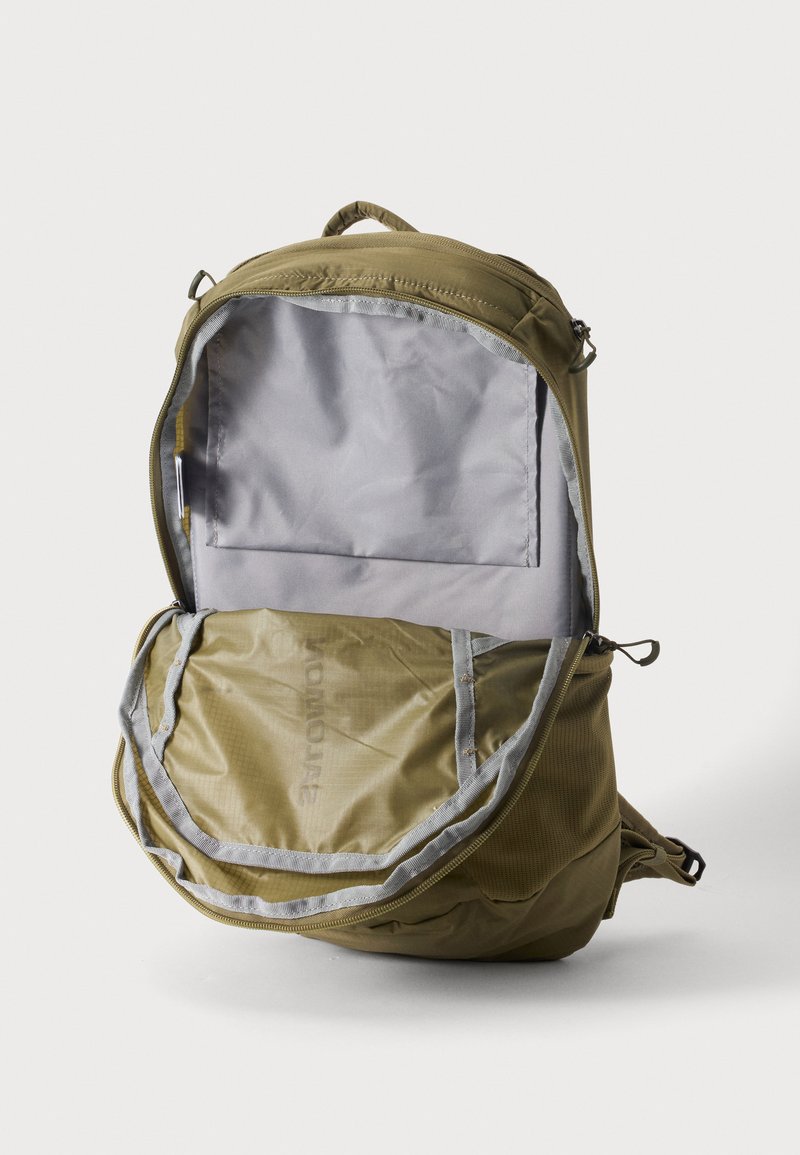 Zaino color sabbia con la cerniera anteriore completamente aperta, che mostra un ampio scomparto principale vuoto e una tasca interna, su sfondo bianco uniforme.
