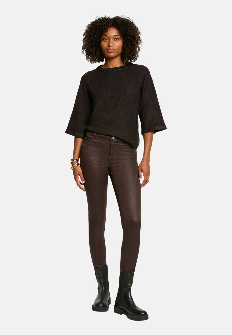 Un pull noir texturé à manches larges, associé à un pantalon en simili cuir marron ajusté et des bottines noires. Les accessoires comprennent des bracelets en or.