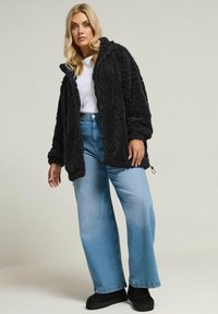 Mustat, tekstuuriset fleece-takit, joissa on vetoketju ja huppu, yhdistettynä vaaleansinisiin, leveälahkeisiin farkkuihin ja mustiin nilkkurit.