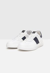 Sneaker bianche in pelle con una striscia blu, dettagli texture, lacci piatti e una robusta suola bianca; presenta un branding minimale sulla linguetta.