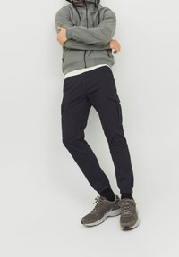 Marinkraftbyxor med elastiska muddar, utrustade med två sidofickor och en stilren design, kombinerat med en grå zip-up jacka och sportiga skor.