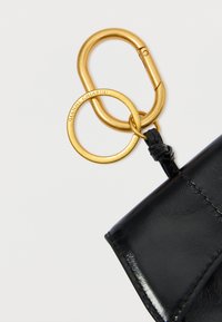 Sort læderpung med gul metalhardware, der har to sammenkoblede ringe og en lille læderdetalje. Glat tekstur.