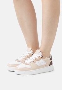 Beežid ja valged nahast sneakerid tekstureeritud viimistlusega, ümmarguse varbaga, jooksva ninaga esiosa ja pruuni aktsendiga kannal.