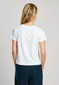 Wit katoenen t-shirt met korte mouwen, een ronde hals, een gladde textuur en rechte snit, gecombineerd met donkerblauwe broeken.