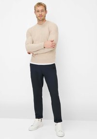 Beiger Pullover mit langen Ärmeln, kombiniert mit marineblauen Slim-Fit-Hosen und weißen Turnschuhen. Der Pullover hat einen Rundhalsausschnitt und eine dezente Struktur.