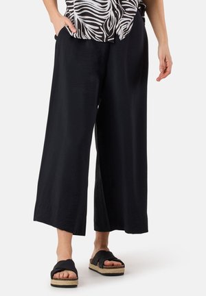 Black wide-leg pants made of lightweight material, featuring a smooth texture and side pockets, paired with black platform sandals.