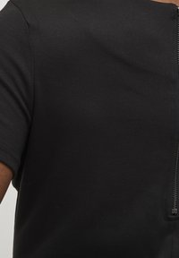 Svart kortärmad topp i slät tyg, med en dold dragkedja på baksidan. Minimalistisk design med en kroppsnära silhuett.