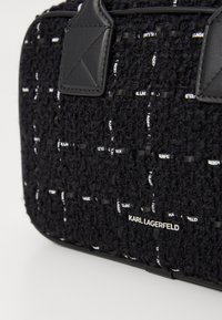 Μαύρη τσάντα tote με υφή από πλεκτό ύφασμα και δερμάτινες λεπτομέρειες. Διαθέτει λογότυπο σε λευκό χρώμα και δομημένο σχήμα.