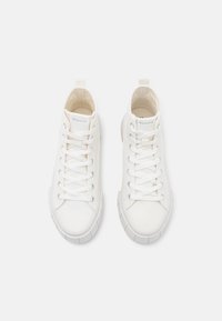 Een paar witte hoge canvas sneakers met witte veters en rubberen zolen, vanuit bovenaf bekeken op een effen achtergrond.