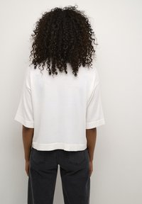Top corto bianco a maniche corte con orlo arrotondato e tessuto texturizzato, abbinato a jeans a vita alta grigio scuro. Vista posteriore mostrata.