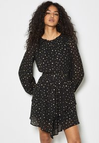 Schwarzes Chiffonkleid mit langen Ärmeln, rüschigem Halsausschnitt, goldenem Sternenmotiv und schichtartigem Rockdetail. Tailliertes Design, fließende Silhouette.