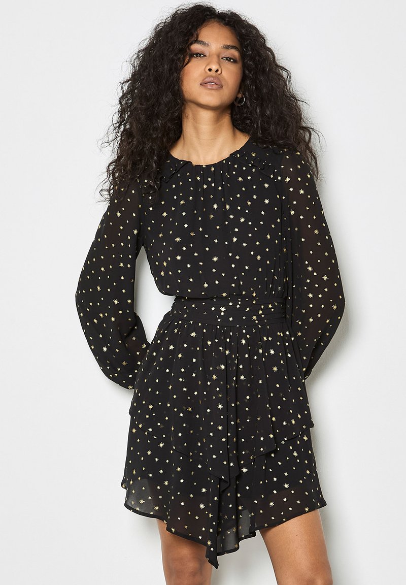 Schwarzes Chiffonkleid mit langen Ärmeln, rüschigem Halsausschnitt, goldenem Sternenmotiv und schichtartigem Rockdetail. Tailliertes Design, fließende Silhouette.