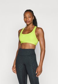 Sostenedor deportivo verde brillante con escote en forma de scoop y un logo blanco de Nike, combinado con mallas de cintura alta con estampado de leopardo negro.