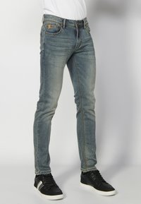 Slim fit traperice u izblijedjelom plavom denimu sa suptilnim izblijeđenjem. Imaju pet džepova, kontrastne šavove i petlje za pojas. Uparene su s crnim tenisicama.