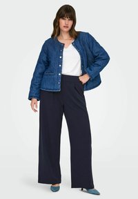 Prošívaná džínová bunda v tmavě modré barvě se zaklapávacími knoflíky, spojená s kalhotami širokého střihu v námořnické modři. Pod tím bílá košile a k tomu špičaté tyrkysové lodičky.