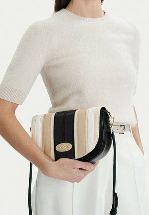 Vrouw draagt een wit kort mouwen truitje en broek, met een zwarte, crèmekleurige en beige gestreepte crossbodytas met gouden hardware.