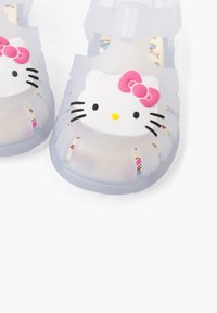 Clear plastic sandals featuring a white Hello Kitty design with a pink bow, open-toed, and lined with a colorful patterned insole.