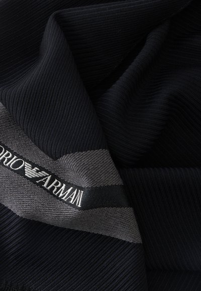 Tissu côtelé noir et gris avec une étiquette tissée affichant le nom de la marque "Emporio Armani" en texte blanc.