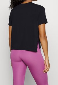 Camiseta negra de manga corta con un corte holgado, cuello redondeado y aberturas laterales, combinada con leggings rosas ajustados y suaves.