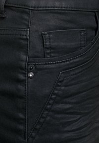 Pantalones vaqueros de mezclilla negra con una textura suave, detalles de costura sutiles y un pequeño botón de metal en el bolsillo delantero.