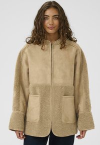 Tanha nahast ja karusnahast jope pikkade varrukatega, esikruviga ja kahe taskuga. Pehme tekstuur ja lõdvestunud istuvus.