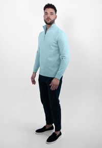 Lichtblauwe, ritssweater van zacht breisel, gecombineerd met een donkere broek en zwarte instappers. Eenvoudig ontwerp en geribbelde manchetten.