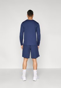 Marineblå langermet skjorte kombinert med matchende shorts, med en avslappet passform. Hvite sportssko og sokker fullfører antrekket.