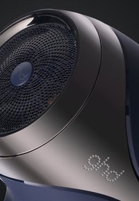 Gros plan sur un haut-parleur noir et argenté élégant avec une grille perforée et un logo bleu au centre, le tout sur un fond sombre.