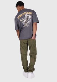 Gray graphic t-shirt featuring an eagle design and "DROPSIZE" text on back, paired with olive cargo pants and white sneakers.