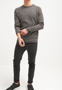 Pull en laine grise avec col et poignets côtelés, associé à un jean noir déchiré et des baskets noires avec des semelles blanches.