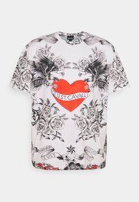 Vit T-shirt med svarta rosillustrationer, två svarta örnar på vardera sidan av ett rött hjärta, och "Just Cavalli"-text på en banner över hjärtat.