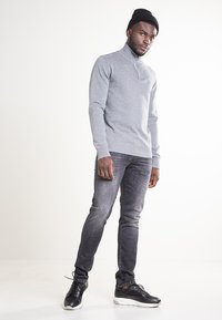 Szary, dziergany sweter z wysokim kołnierzem, zestawiony z ciemnoszarymi dżinsami i czarnymi tenisówkami. Gładki kolor, miękka faktura i dopasowany fason.