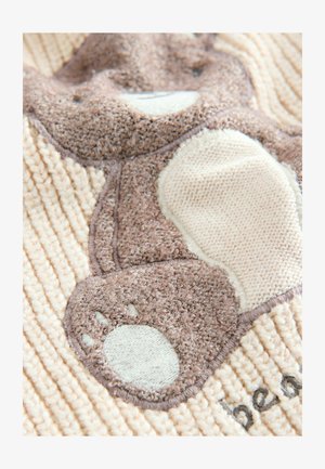 Švelnus smėlio spalvos audinys su lokio dizainu rudais atspalviais, turintis tekstūrinius elementus ir kontrastingas siūles. Įtrauktas akcentinis lokio pėdutės atvaizdas.