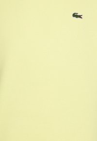 Ljusgul bomulls-T-shirt med ribbad textur. Har en liten grön krokodillogo på vänster bröst. Enkelt och avskalat design.