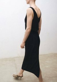 Black sleeveless dress with a V-back, featuring a flowy skirt. Worn with high-heeled shoes in a snake print pattern. Smooth fabric texture.