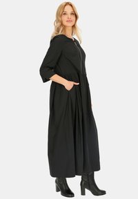 Czarna midi sukienka z zamkiem z przodu, rękawami o długości trzy czwarte i bocznymi kieszeniami. Wykonana z lekkiego materiału, z elastycznym w pasie i zwiewnym dołem.