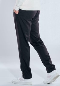 Black trousers with a straight fit, made of smooth fabric, featuring side pockets. Paired with white sneakers for contrast.