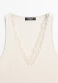 Roomkleurige geribde mouwloze top met diepe V-hals afgewerkt met delicate kanten rand, met label Massimo Dutti.