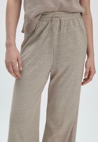 Hellgraue, weit geschnittene Hose aus weichem Stoff. Verfügt über einen elastischen Bund mit Kordelzug und eine glatte Textur.