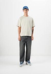 Lys beige oversized t-shirt, grå baggy jeans og blå denimkasket. Hvide sneakers med blå accenter. Enkelt design, ingen mønstre.