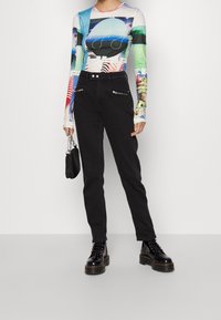 Dlouhý rukáv s barevným grafickým designem; černé kalhoty s kapsami na zip; černé šněrovací boty; malá černá kabelka.