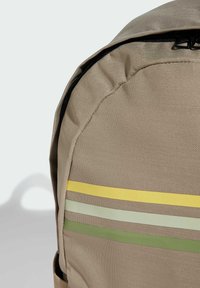 Zaino beige con una texture liscia, caratterizzato da strisce orizzontali verdi, gialle e verde chiaro. Chiusura superiore con cerniera e forma tondeggiante.