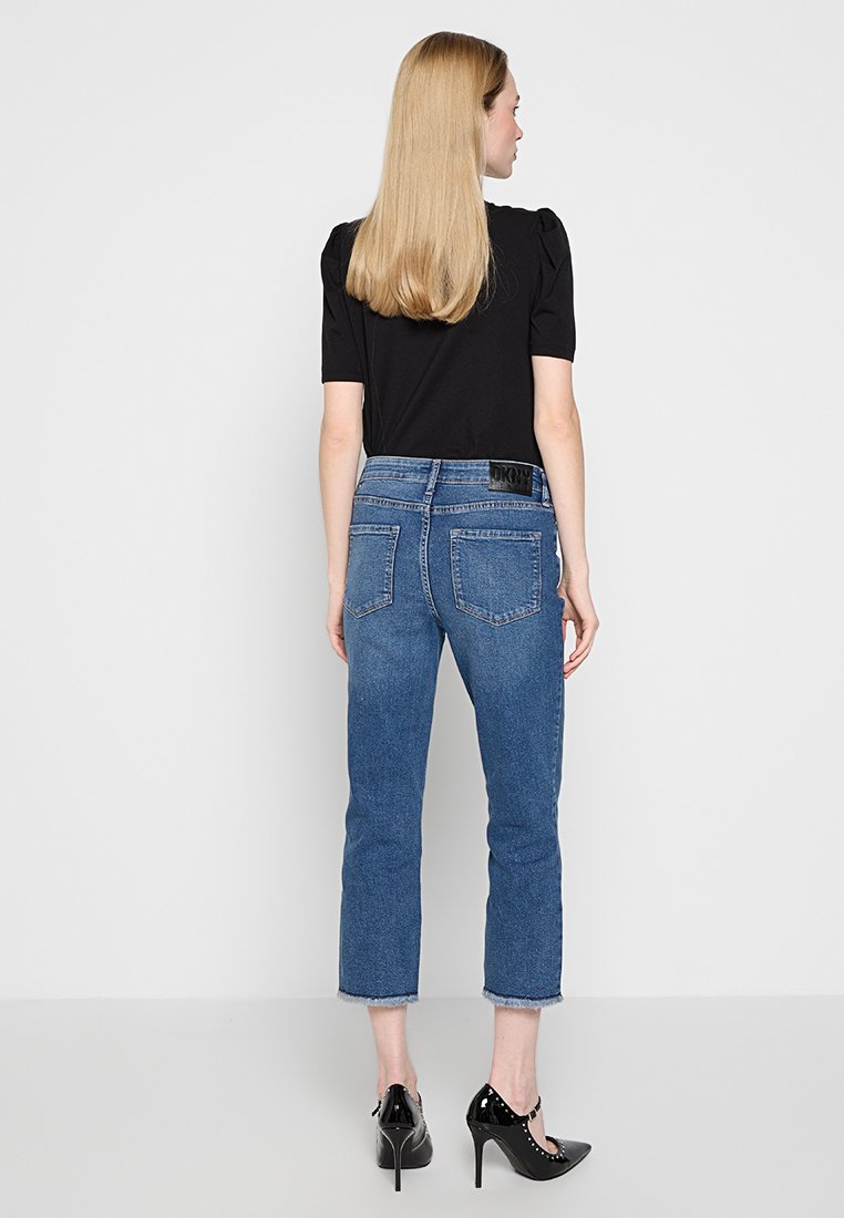 Top corto a maniche corte di colore nero, abbinato a jeans in denim blu con taglio dritto e lunghezza cropped, dotato di una cintura elastica nera con logo. Tacchi alti neri.