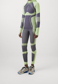 Tajta träningsset i grönt och lila, med texturerad tyg, långa ärmar, huva och meshdetaljer på leggings.