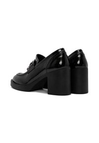 Scarpe con tacco nere in finitura lucida in vernice, con punta arrotondata e tacco a blocco spesso. Dettagli hardware sulla parte superiore.