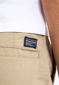 Pantalones beige de algodón con una etiqueta que dice "Petrol Ind." que muestran una forma rectangular y una textura suave.
